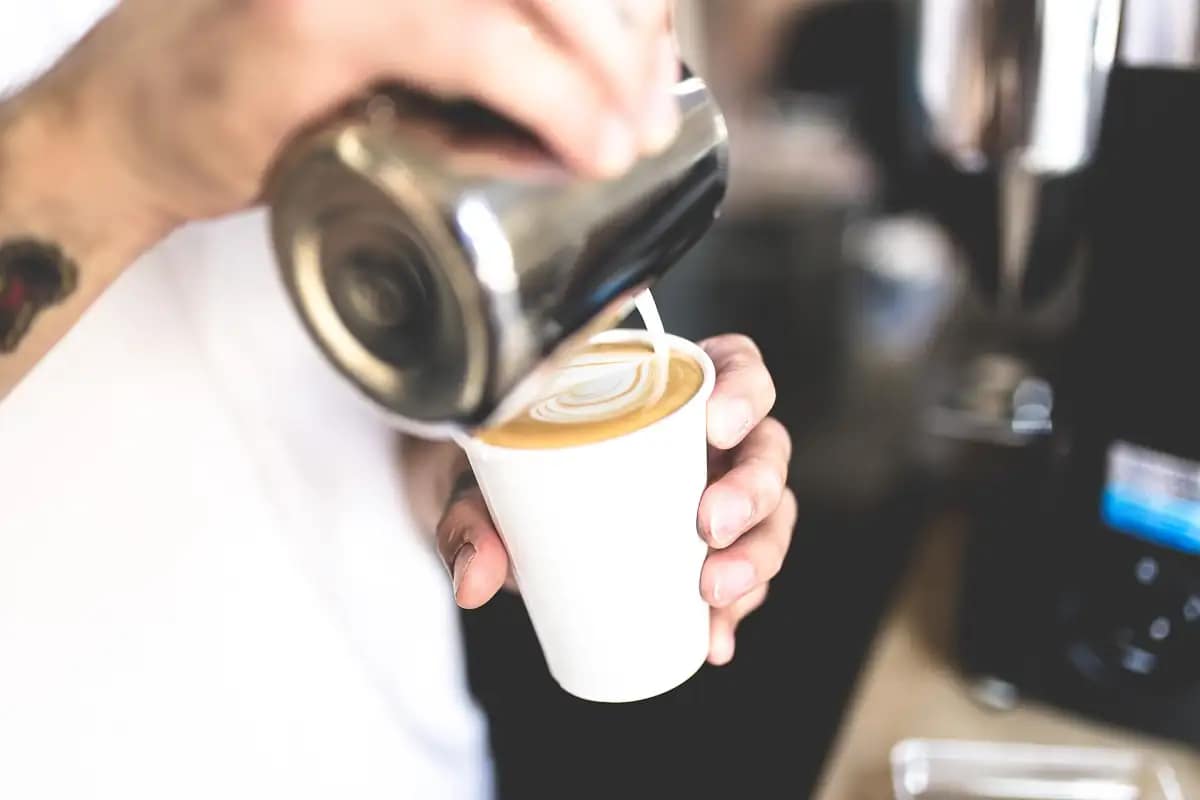 Barista pouring milk into a coffee in an independent café